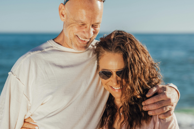 A young couple is embracing and smiling in warm, sunny weather after moving to a warmer climate.