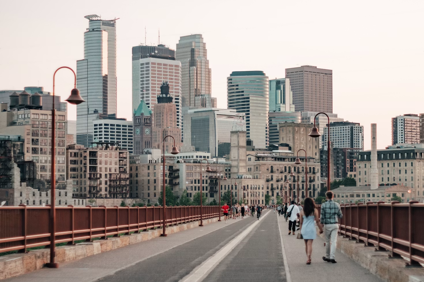People living in Minneapolis enjoy a sunset walk across a city bridge with the Minneapolis skyline in the background.