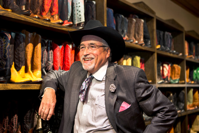 A senior man in a suit and cowboy hat is smiling in a boot store in Texas.