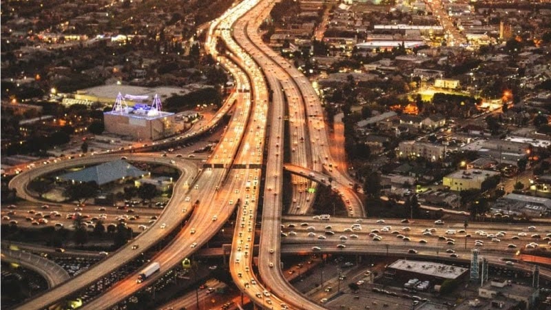 Aerial view of Los Angeles freeways at night, with headlights and street lights casting an orange glow across the concrete.