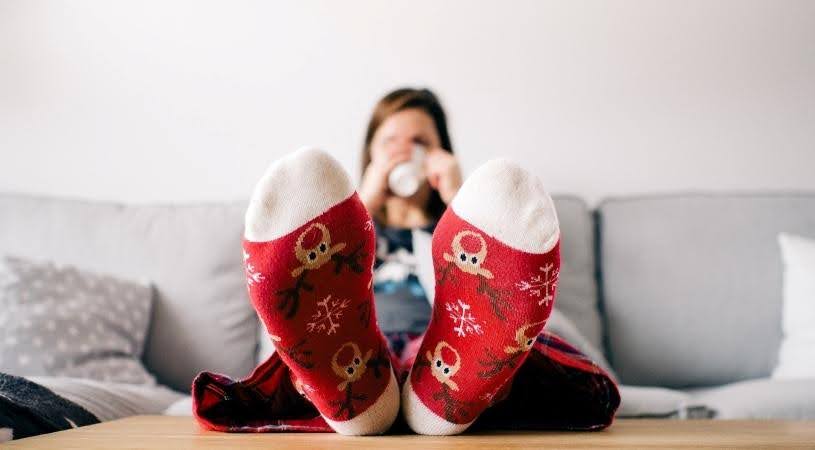 A woman relaxes on the couch in festive socks after finishing her last-minute Christmas gifts.