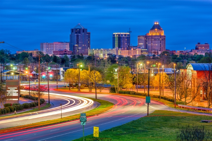 Nighttime view of Downtown Greensboro with glowing city lights and traffic trails leading into one of the best neighborhoods in Greensboro, NC.
