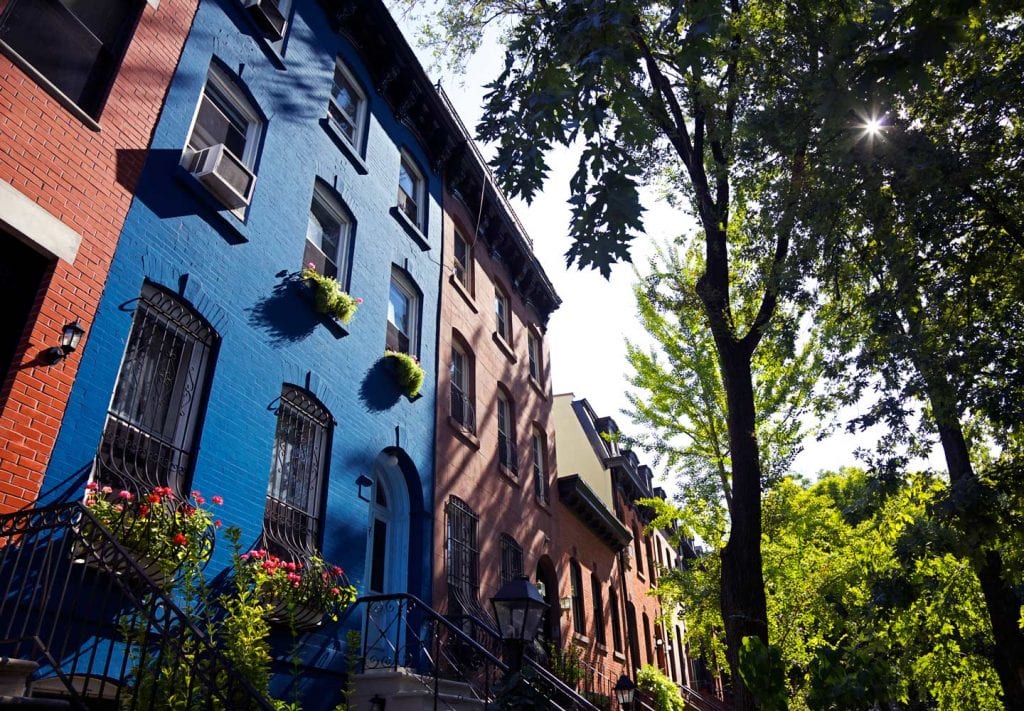 Brownstones lining the streets in one of Brooklyn's neighborhoods. One is painted a rich royal blue, making it stand out from the monotony of red brick facades. You'l