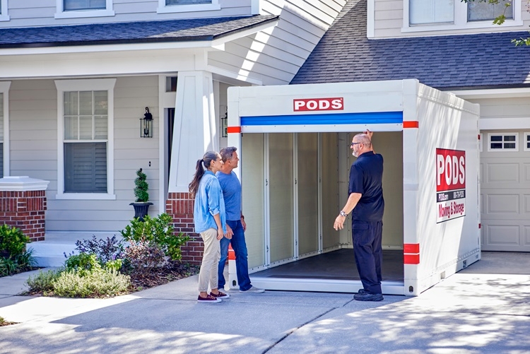 A PODS driver has just delivered a PODS portable storage container to a residential driveway. He has opened the container door and is showing the inside to a mature couple who will be using it for storage. 