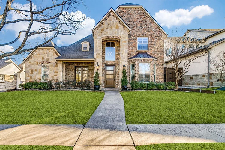 a multi-story stone mansion in the Wilshire Heights neighborhood in Dallas, Texas. There is a lush green yard and bare trees in the yard. 