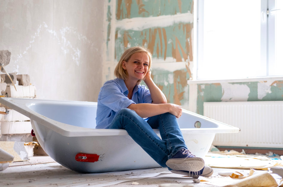 A woman is sitting in a new bathtub in the middle of a bathroom that is mid-renovations