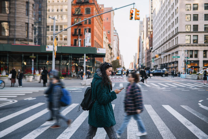Pedestrians cross a street in Manhattan — one of the 5 boroughs of New York — framed by tall city buildings in the background.