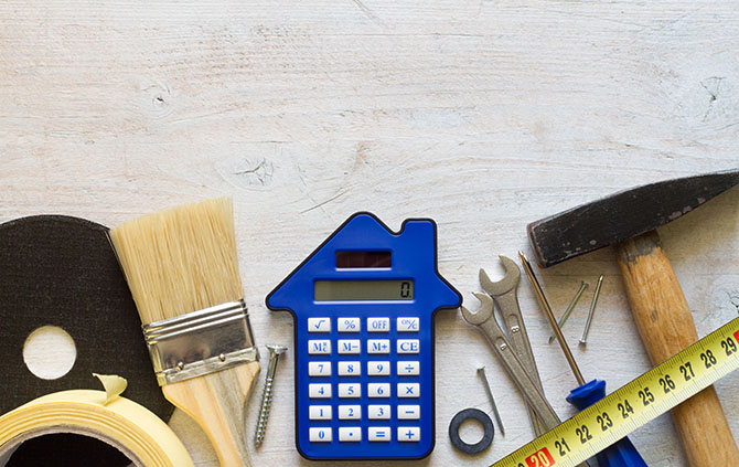 A house-shaped blue calculator with assorted tools lying around it.