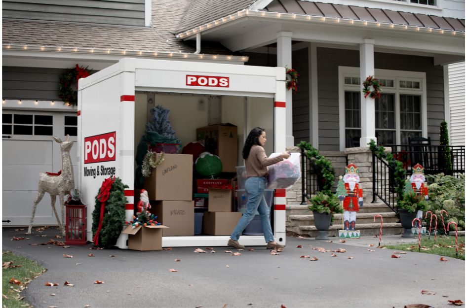 A homeowner declutters by packing and storing Christmas decorations into a PODS portable moving container outside her house.