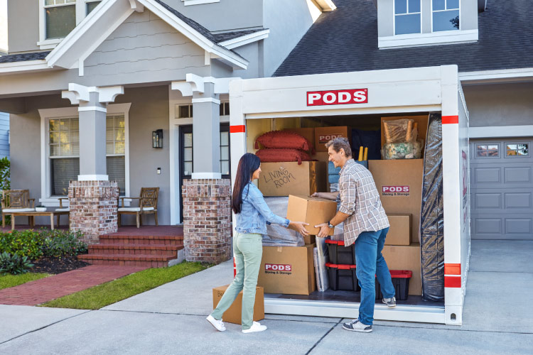 A mature couple is loading the last of their boxes into the PODS portable storage container that sits in their driveway. They’re making a move to Maine, where they’ll spend their retirement years.