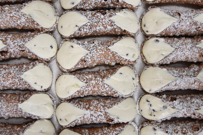Top view of eighteen sugar-dusted cannoli neatly arranged on a baking sheet at Termini Brothers Bakery in Philadelphia.