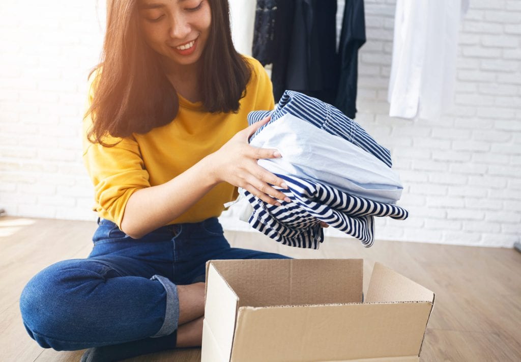 A young woman is using a cardboard box for storing clothes between seasons