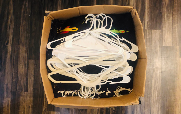 Top-side view of an open moving box, filled with miscellaneous items and topped with a bunch of hangers to add stability.