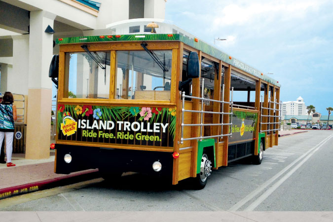 The colorful Pensacola Beach Island Trolley is parked  on a city street waiting for passengers to board.