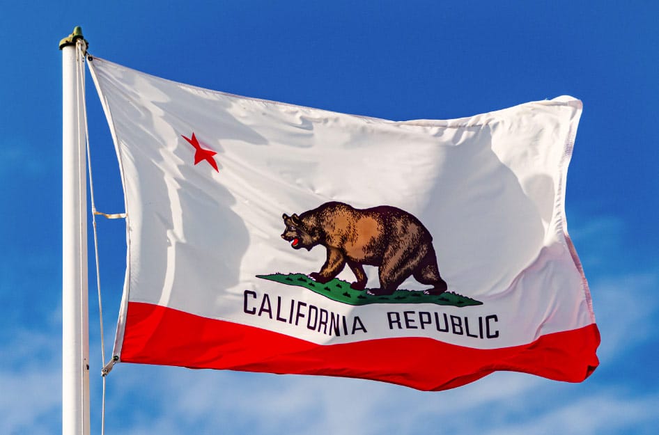 The California state flag flying in front a blue sky