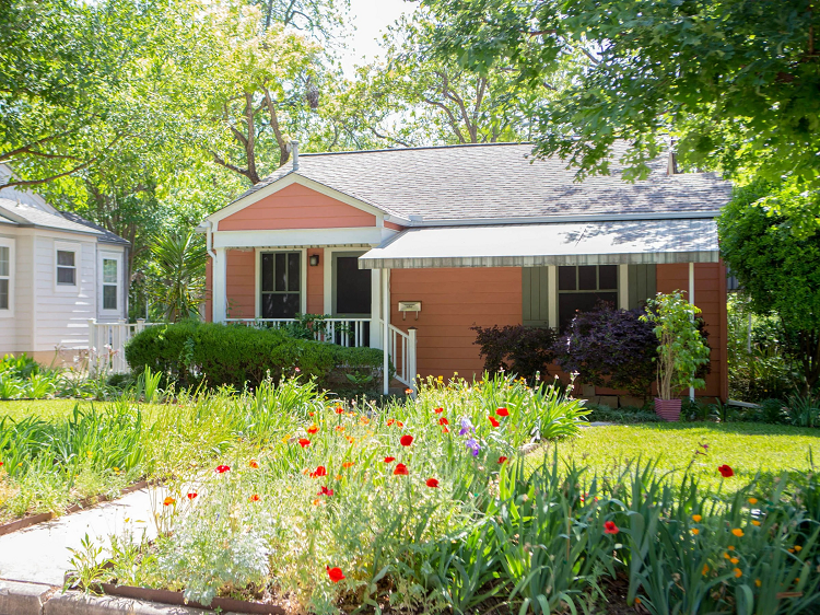 A red one-story home in the Rosedale neighborhood of Austin, Texas, featuring a lush and floral front yard.