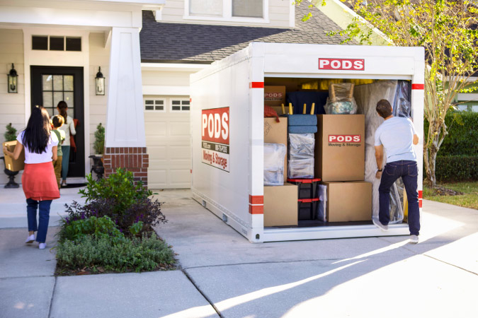 A family of four is unloading a PODS portable moving container in their driveway after moving to Texas.