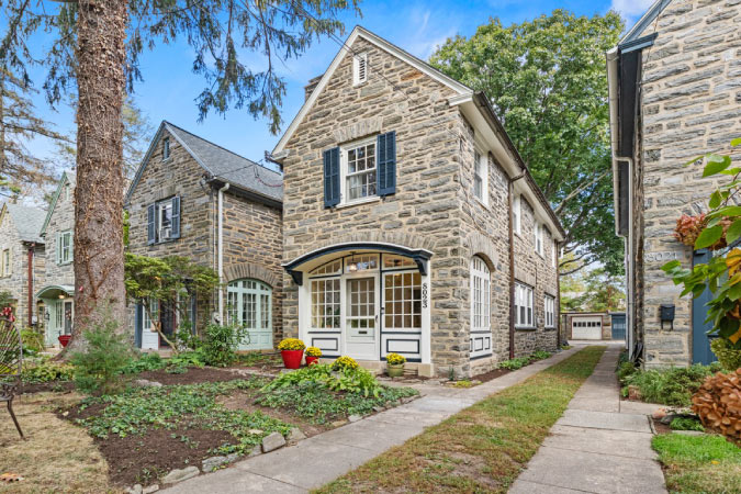  A stone twin home in Chestnut Hill — one of the safest neighborhoods in Philadelphia — featuring a curved awning above the entryway and white and blue accents on the windows.