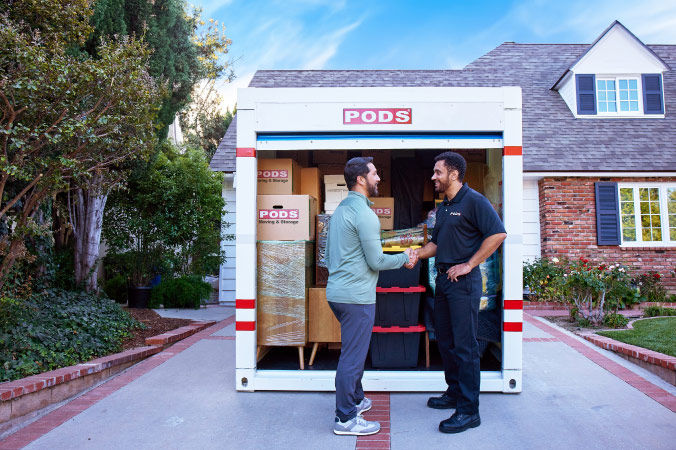 A man is standing in front of a loaded PODS container, shaking hands with a PODS driver.