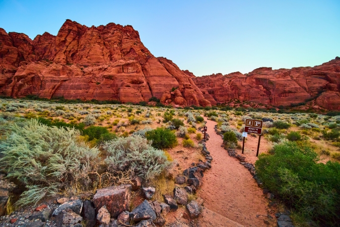 A hiking trail winds its way through a striking desert landscape toward red rock formations in Snow Canyon State Park — one of the many scenic things to do in St. George, Utah.