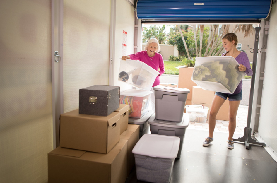 A senior woman and her granddaughter are carrying plastic storage bins into a PODS portable on-site storage container.