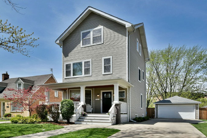 A three-story home with gray siding exterior, detached garage, and a covered front porch, in the Chicago neighborhoods of Norwood Park.