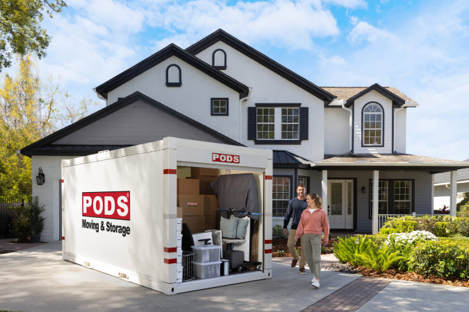 A man and woman are walking beside the loaded PODS portable storage container in the driveway of their home.