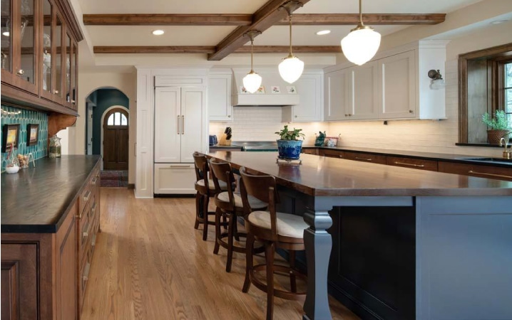 A newly remodeled kitchen featuring pendant lighting above the island dining table, turquoise-colored tile backsplash, and a combination of white-painted and natural wood cabinets.