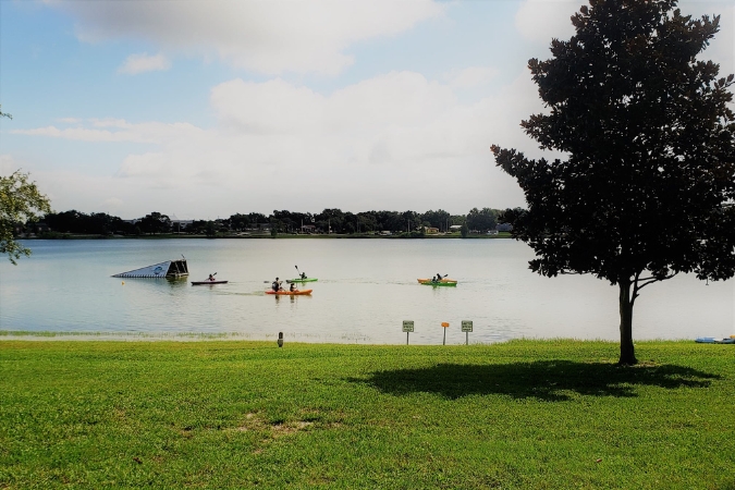 Kayakers living in Lakeland, FL, enjoy a sunny day paddling on the lake with a green park and shady tree in the foreground.