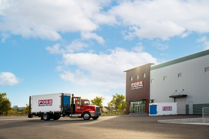 A PODS truck is transporting a portable storage container to a PODS storage facility as part of someone’s job relocation.