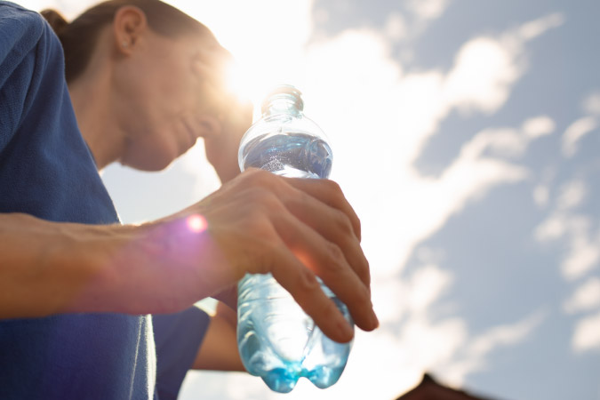 A woman is holding an open bottle of water and shielding her eyes from the bright summer sun in Dallas, Texas
