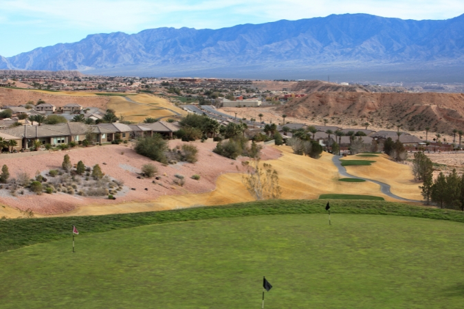 Golf course fairways wind through a residential community in Mesquite, NV, surrounded by ranch-style homes, desert terrain, and mountain views.