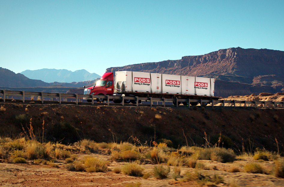 A PODS truck with several containers drives along a highway while completing a long distance move.