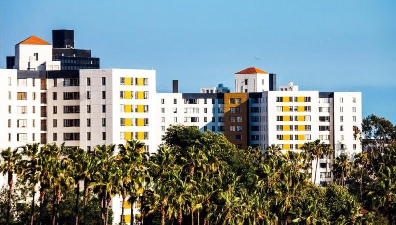 A large apartment complex in Los Angeles set between a grove of palm trees and a clear blue sky.