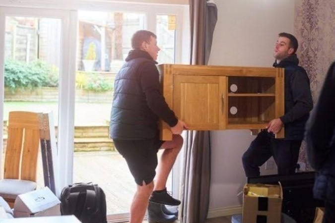 Two professional full-service movers are carefully lifting a piece of furniture, following safety tips about moving.