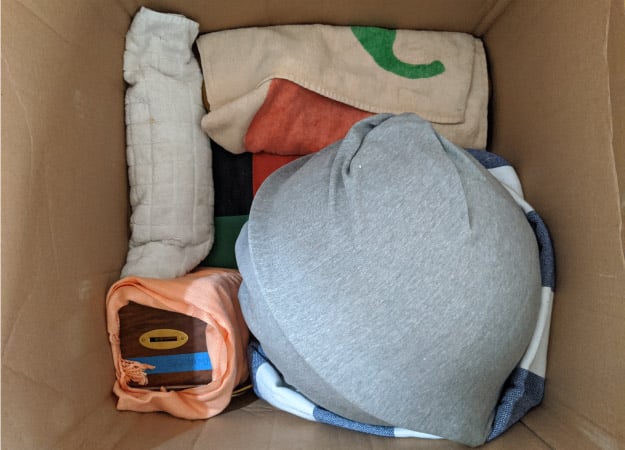 View from above of several fragile items that have been wrapped in clothing and towels and packed snugly inside a box — a cost-effective packing tip for protecting your belongings during a move. 