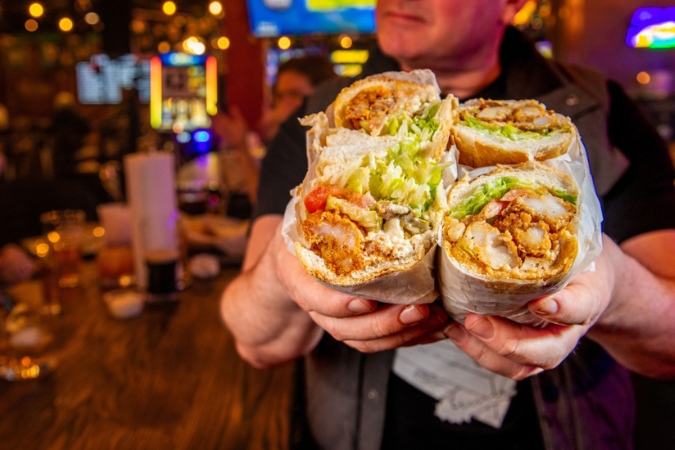 A man in a restaurant holds two shrimp po’boys sliced in half at The Po’Boy Shop and Basement Bar — one of the best restaurants in Decatur, GA.