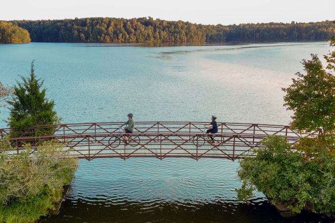 A couple cycles over a bridge, surrounded by water in the Winston-Salem area.