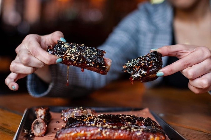 Jersey City neighborhoods include Hamilton Park, where a guest holds a barbecue rib over a plate of ribs at Hamilton Pork.