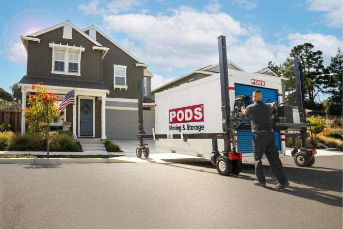 A PODS driver is using PODZILLA to maneuver a PODS portable storage container into place in a residential driveway.