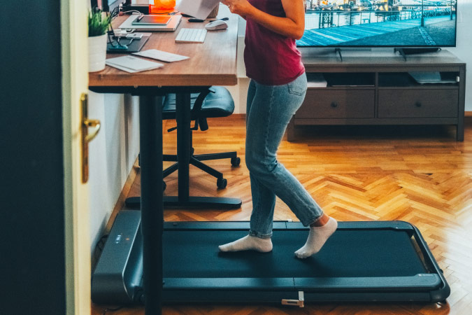 Closeup of a woman walking on a treadmill at her standing desk, part of her home office setup that keeps her moving even while on the computer.
