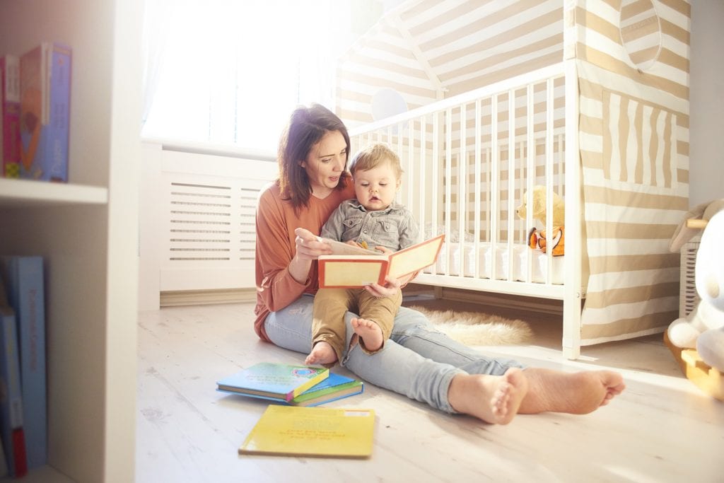 A mother holds her baby in her arms, reading him a storybook