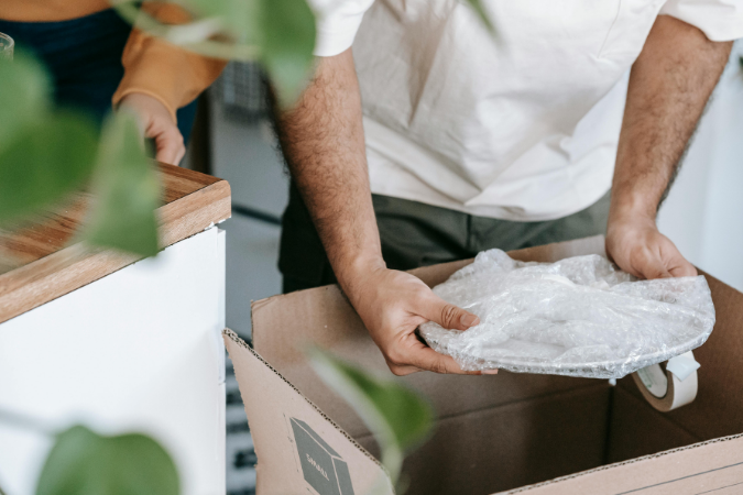 Close up of a man who is packing a dish covered in bubble wrap. This is a great way to pack boxes for moving.