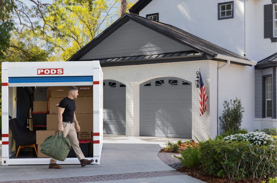 U.S. service member unloading belongings from a PODS portable moving container outside a home during a PCS move.