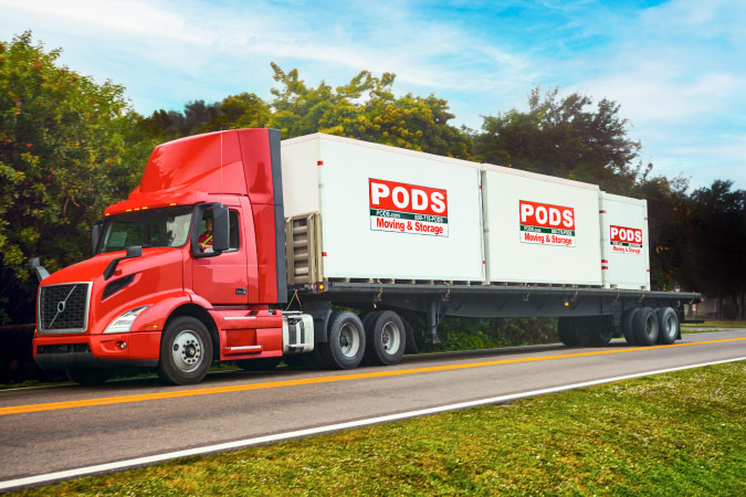 A PODS truck transporting three portable moving containers on a freeway