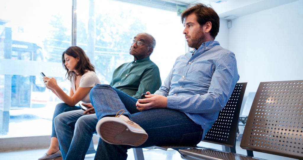 Three people are sitting in the waiting area of their local DMV.