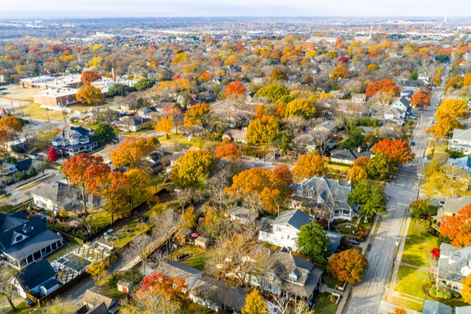 An aerial view of a neighborhood in McKinney, TX — one of the safest cities in the U.S. — featuring two-story houses and fall foliage.