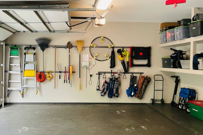A neatly organized garage with tools, ladders, and equipment hung along the walls and stored on overhead shelves — a great example of how to declutter a storage space.