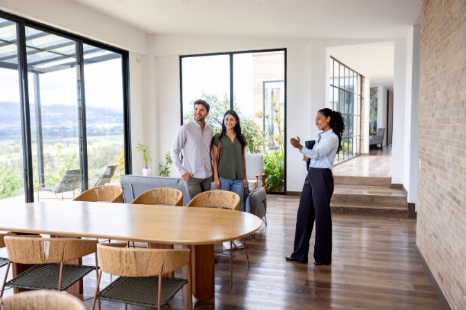A real estate agent is giving a couple a tour of a modern home, illustrating the “home search” step on a first-time home buyer timeline.
