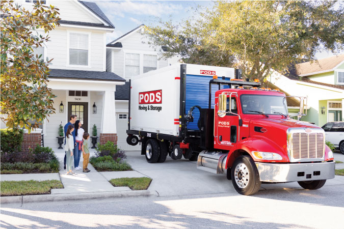  A family looks on as their PODS portable container gets loaded onto the truck. There is a mom, dad, and two kids standing in front of a white home.